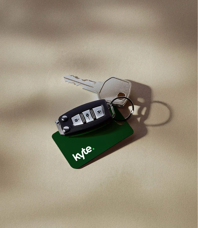 Car keys with a green Kyte keyring on a sunlit neutral surface